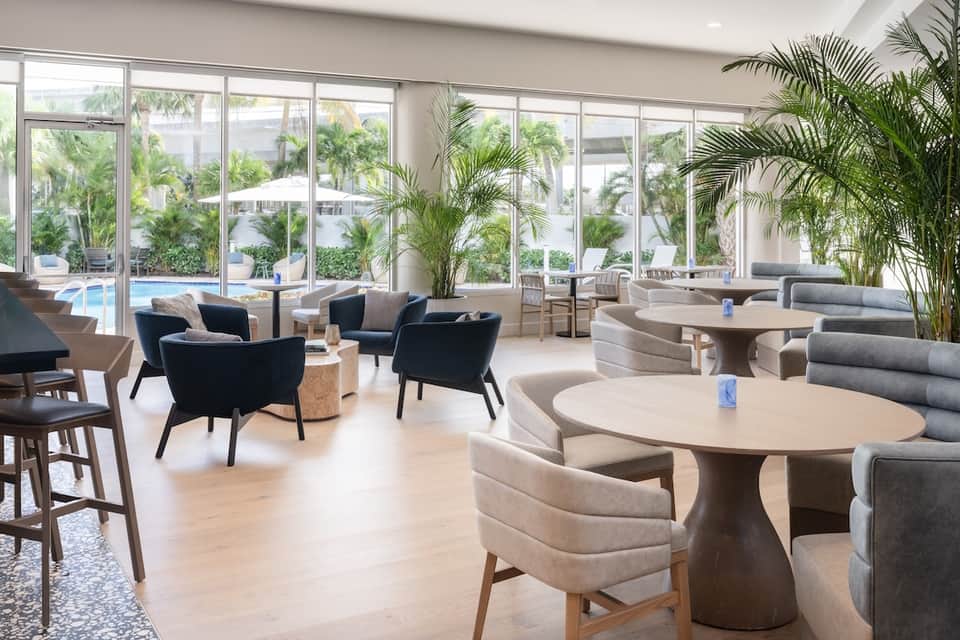 Contemporary hotel lobby and lounge with modern furniture, large windows, and views of palm trees