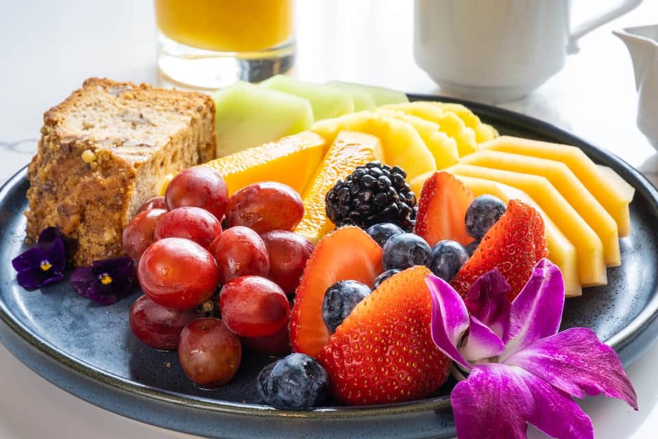Breakfast plate with toast, cheese, fresh berries, grapes, orange juice, and coffee on dark plate