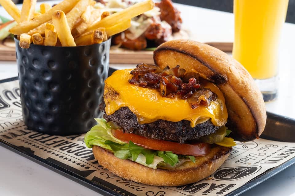 Gourmet cheeseburger with bacon and fries served on branded placemat with beverage