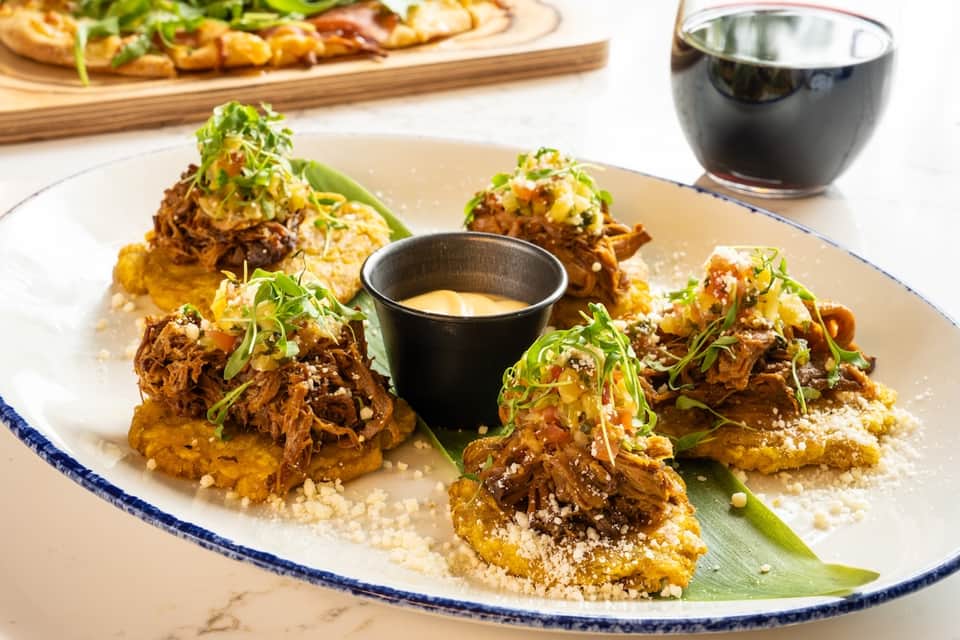 Gourmet appetizer plate with shredded meat, crispy base, green garnish, and dipping sauce