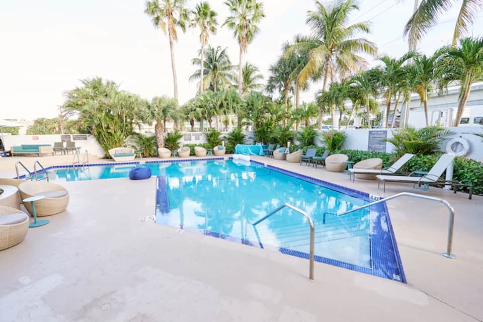Resort pool with crystal blue water, loungers, palm trees, and multi-story beige building