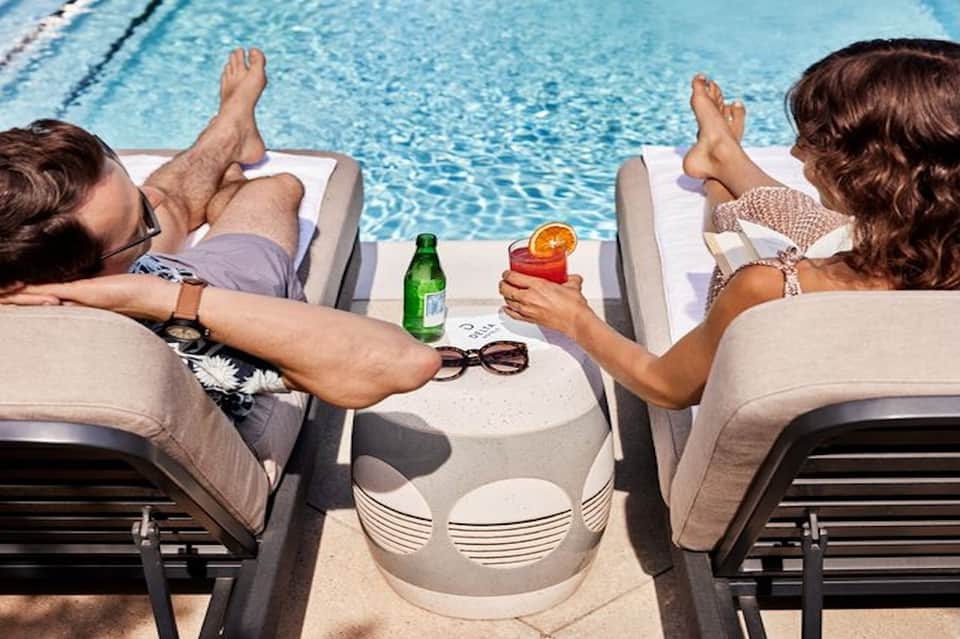 Two guests relaxing on lounge chairs by swimming pool with cocktails