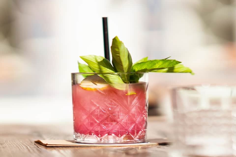 Colorful cocktail with mint garnish and black straw in crystal glass on white surface