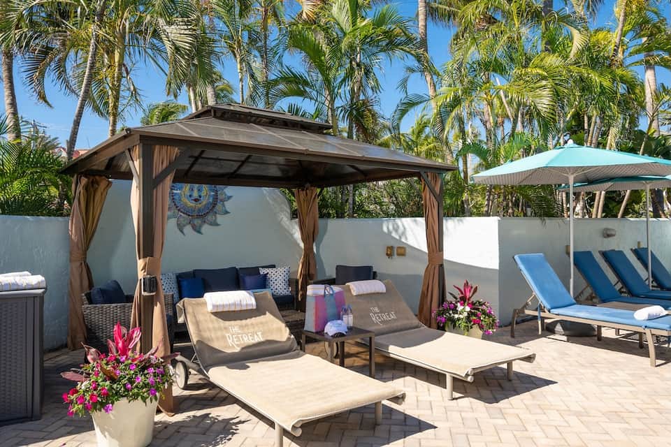 Poolside cabana lounge area with palm trees, comfortable seating, and ocean views in background