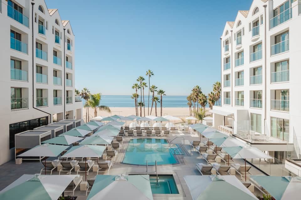 Beachfront resort pool area with turquoise umbrellas, loungers, and ocean view between buildings