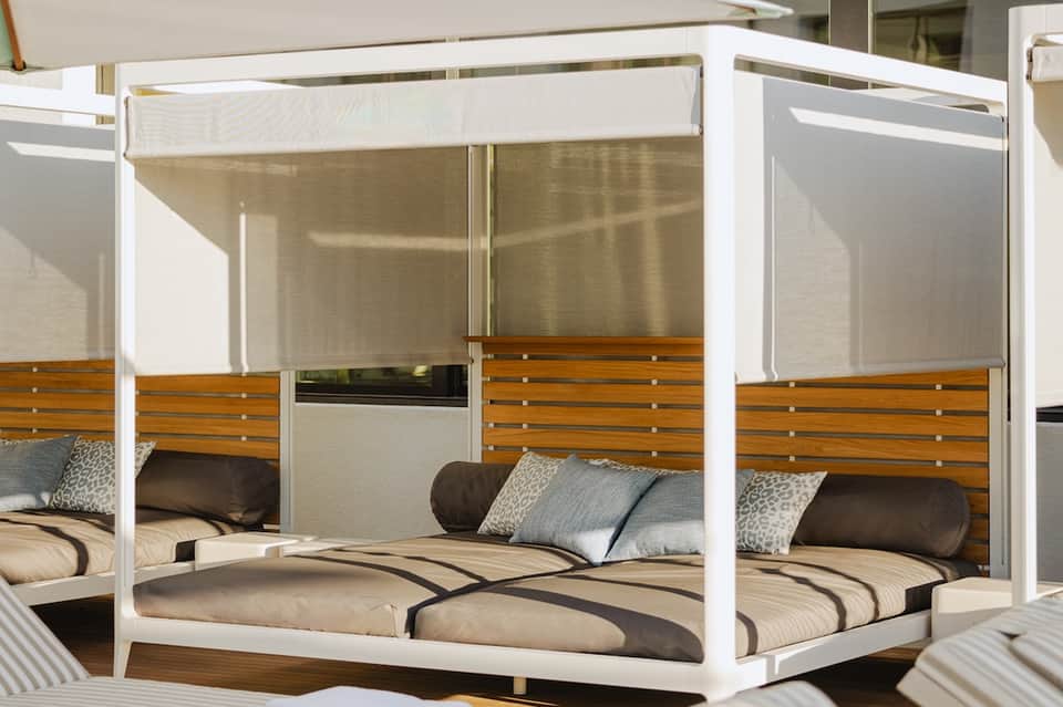 Modern white canopy bed with wooden trim and striped bedding on outdoor terrace