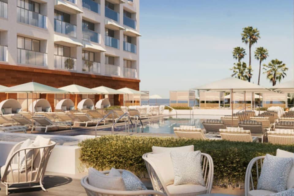 Beachfront resort pool deck with lounge chairs, umbrellas, palm trees, and modern hotel building facade