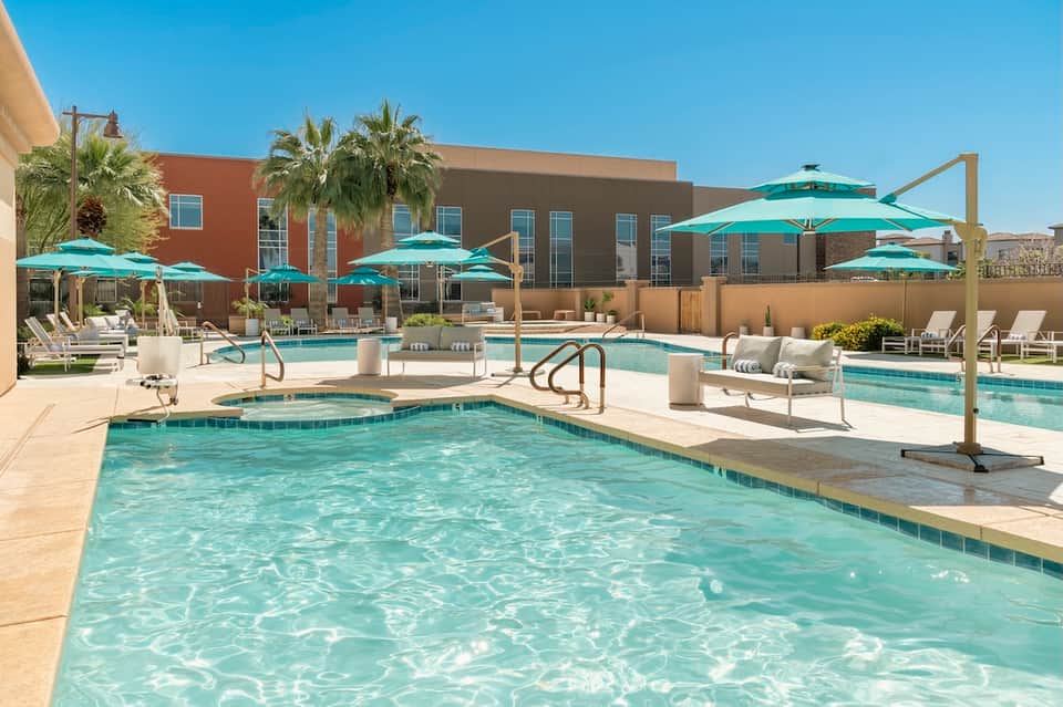 Outdoor pool complex with spa, turquoise umbrellas, white lounge chairs, and desert landscape