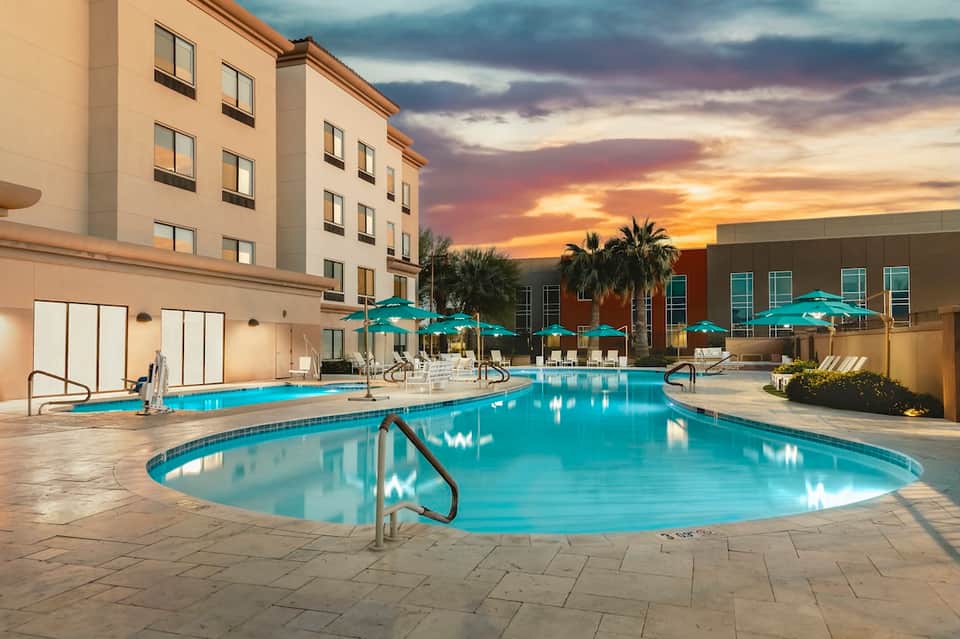 Illuminated resort pool deck at dusk with palm trees and hotel building