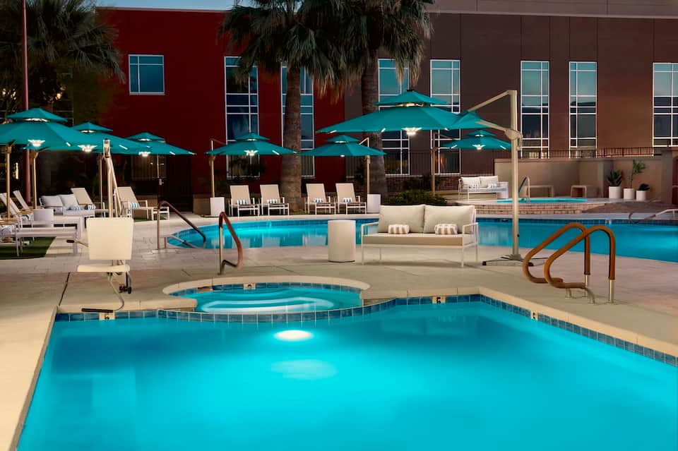 Resort pool area with turquoise water, teal umbrellas, lounge chairs, and modern building