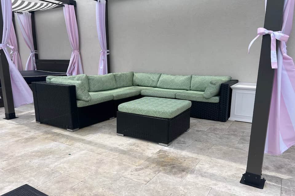 Outdoor lounge seating with black rattan sectional, green cushions, and purple curtain drapes