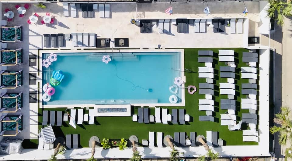 Aerial view of rectangular pool surrounded by white and gray loungers on manicured lawn