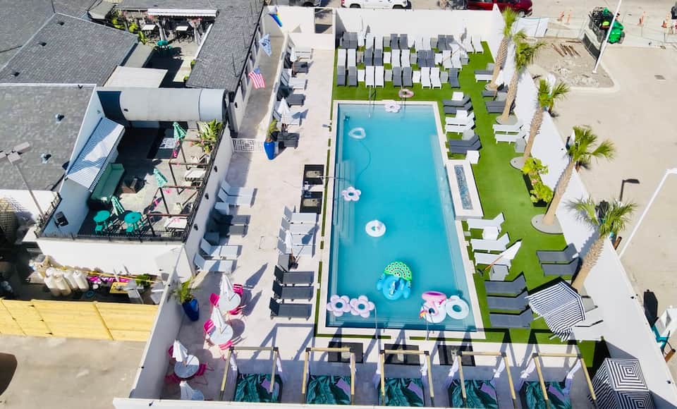 Aerial view of modern beachfront resort with rectangular pool, white cabanas, and manicured green lawn
