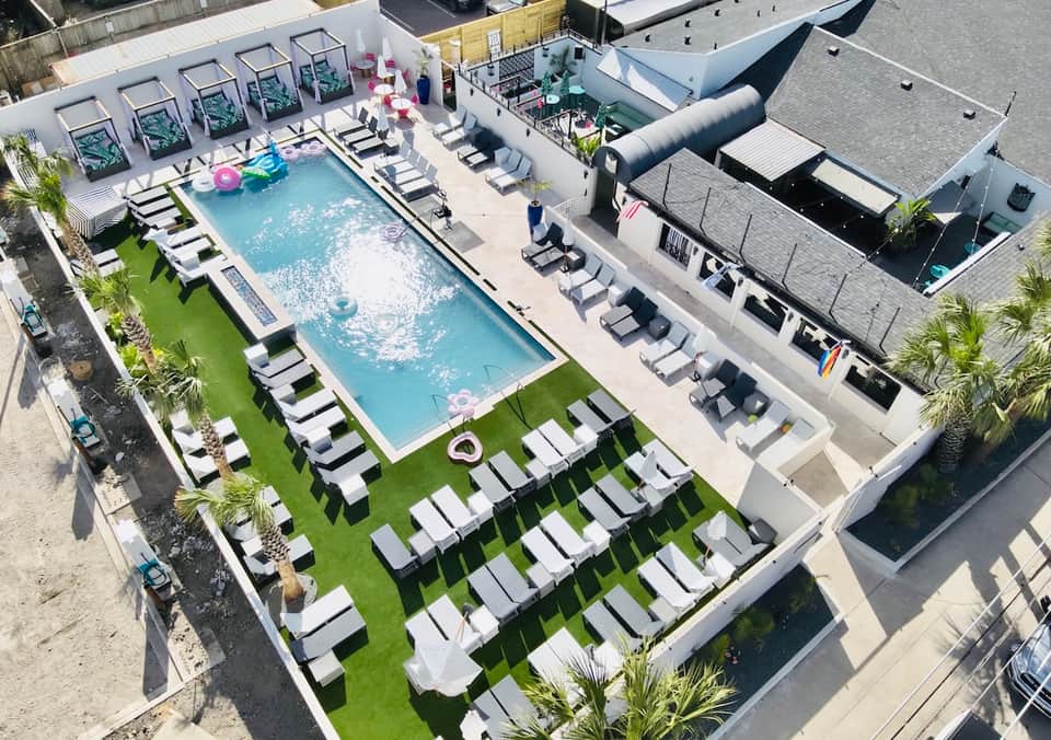 Aerial view of resort pool deck with white lounge chairs, green lawn, and modern buildings