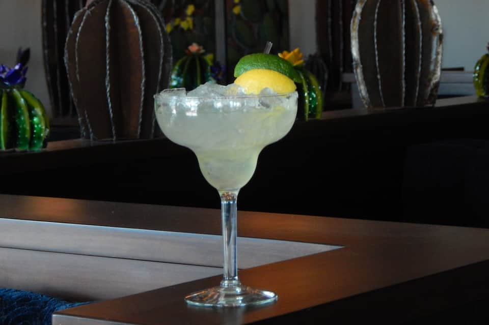 Margarita cocktail with lime and salt rim on bar counter with cactus decorations in background