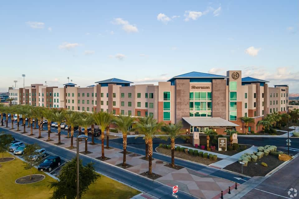 Sheraton hotel exterior with tan and coral facade, blue roofs, palm trees, and parking lot