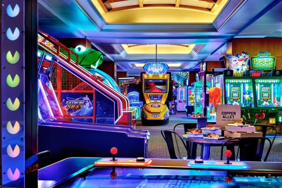 Colorful arcade and game room with neon-lit gaming machines, air hockey table, and vibrant lighting throughout