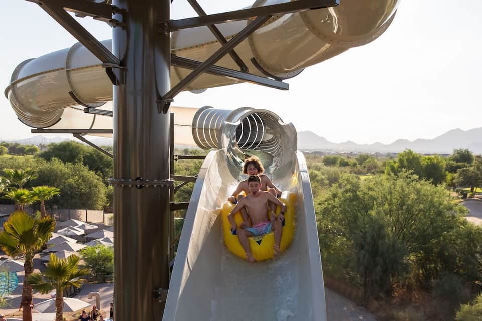 Children on a twisting water slide at a resort with desert landscape and palm trees visible