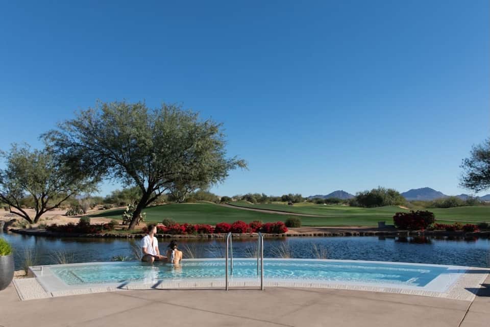 Resort pool overlooking golf course with mountains, desert landscaping, and clear blue sky