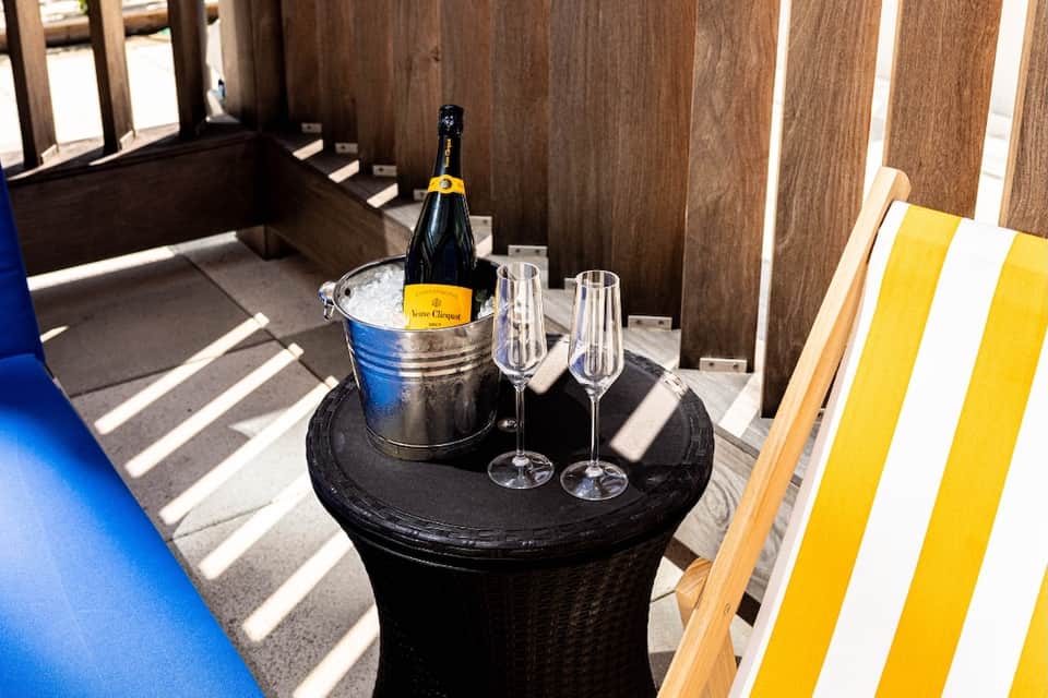 Champagne bottle in ice bucket with glasses on round table in wooden cabana
