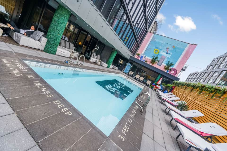 Urban rooftop pool with light blue water, deck lounge chairs, and surrounding high-rise buildings