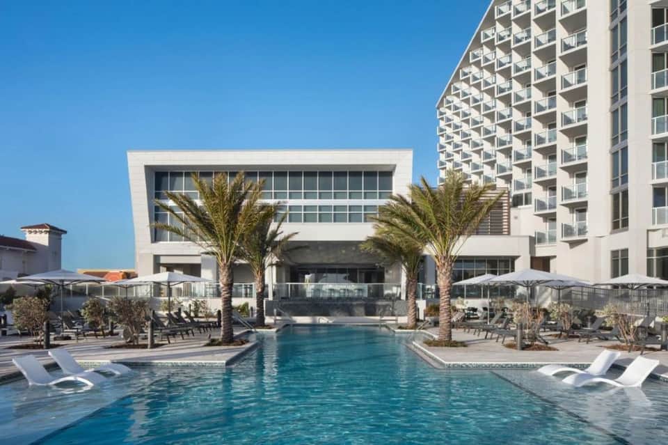 Resort outdoor pool with palm trees, loungers, and multi-story hotel building in clear daylight