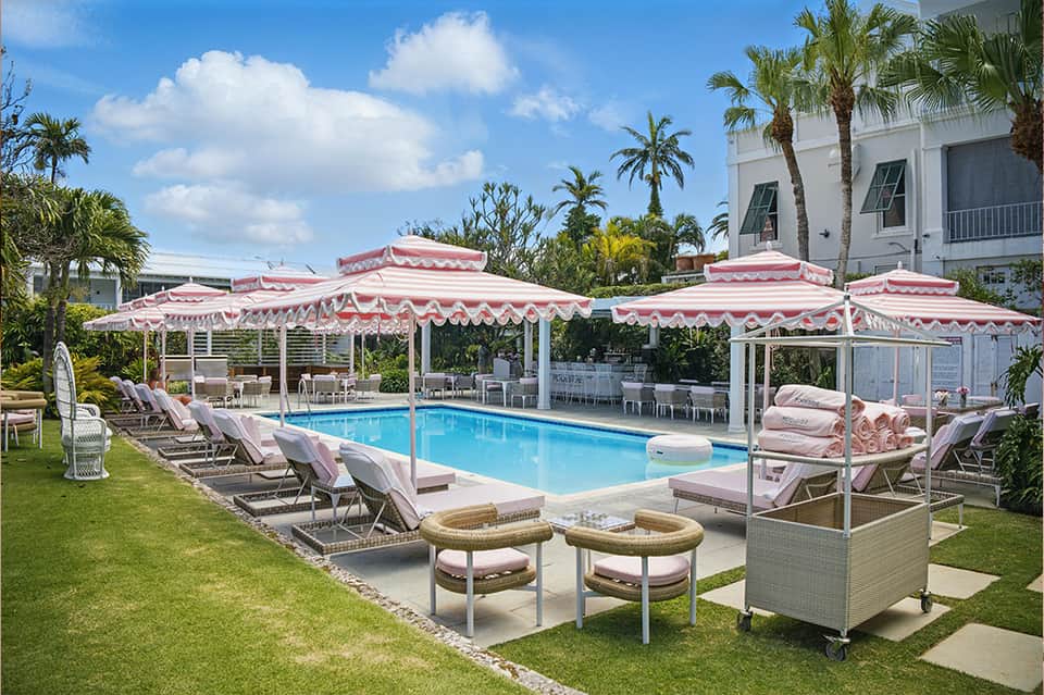Elegant pool area with pink and white striped umbrellas, lounge chairs, and manicured lawn