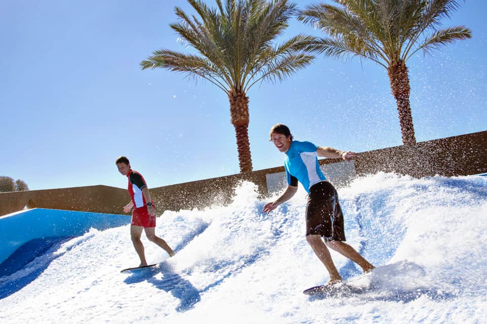 Children playing on artificial wave slides under palm trees in bright sunshine