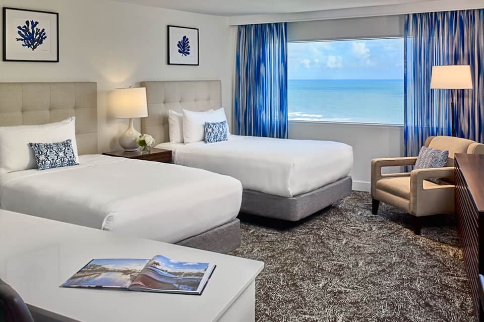 Beachfront hotel room with two queen beds, ocean view, blue curtains, and modern décor