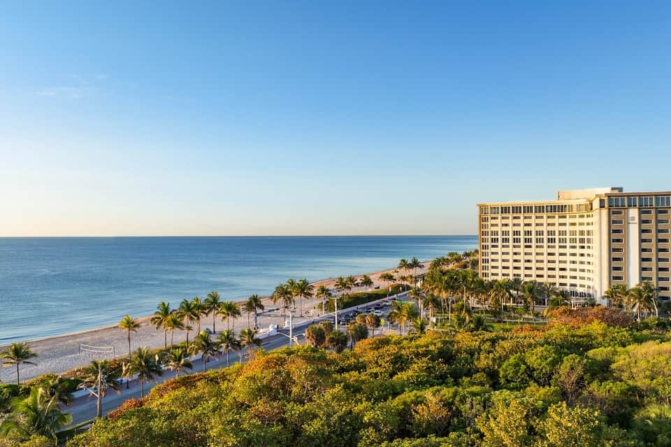 Beachfront resort hotel overlooking sandy beach, palm trees, and calm blue ocean waters