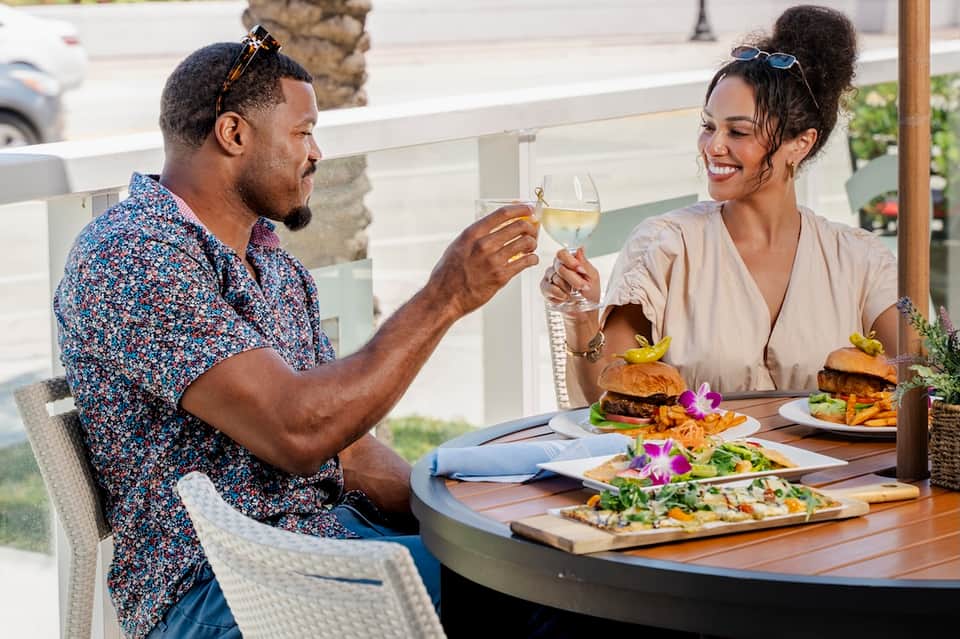 Couple toasting with white wine at outdoor dining table with burgers and salads