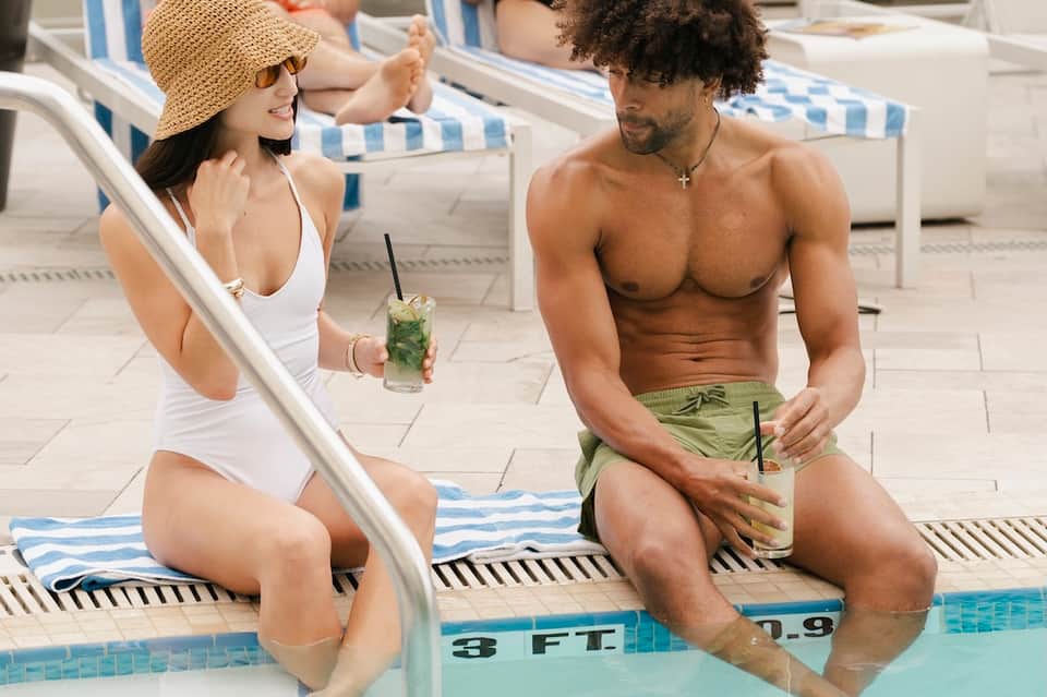 Couple at poolside in swimwear enjoying drinks and conversation by the water