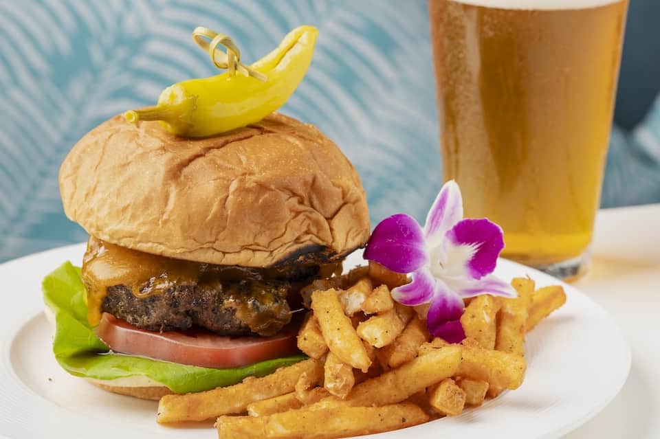 Gourmet burger with fries and beer served poolside with tropical flowers