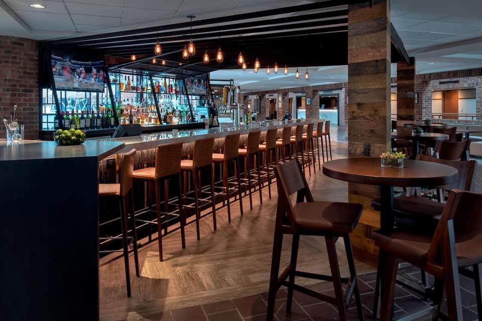 Modern hotel bar with dark wood counter, copper pendant lights, brick walls, and wooden flooring