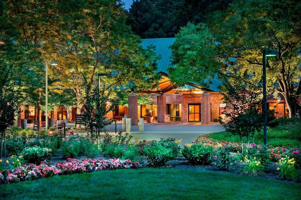Brick resort building with blue roof reflected in pond, surrounded by landscaped gardens and trees
