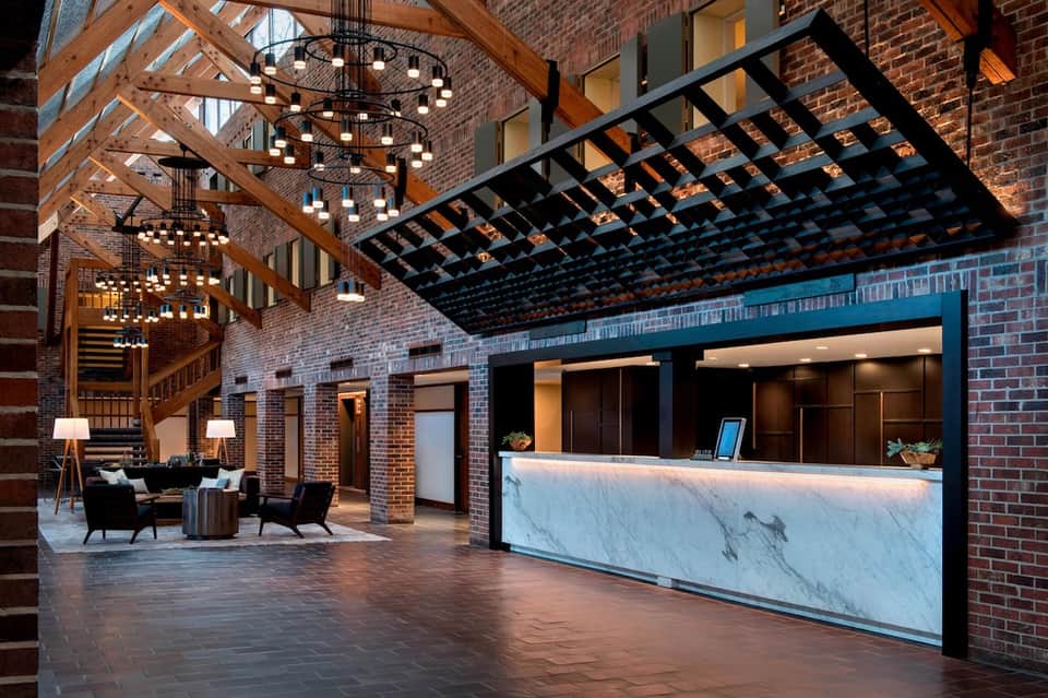Modern hotel lobby with exposed brick, wooden beams, marble reception desk, and chandeliers