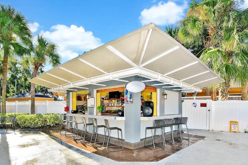Casual outdoor bar with retractable awning, palm trees, and white picket fence