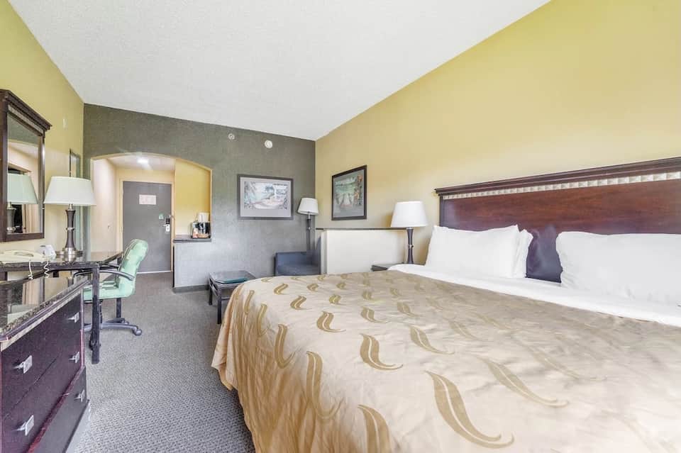 Hotel bedroom with queen bed, work desk, yellow and gray walls, and bathroom entrance