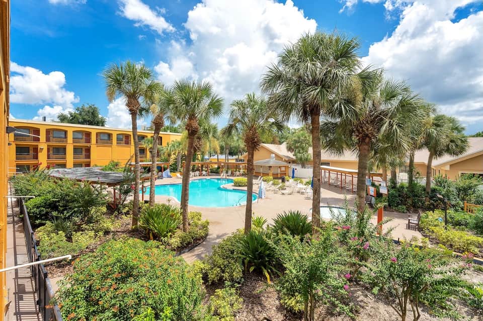 Resort courtyard with swimming pool, tall palm trees, yellow building, and lush landscaping