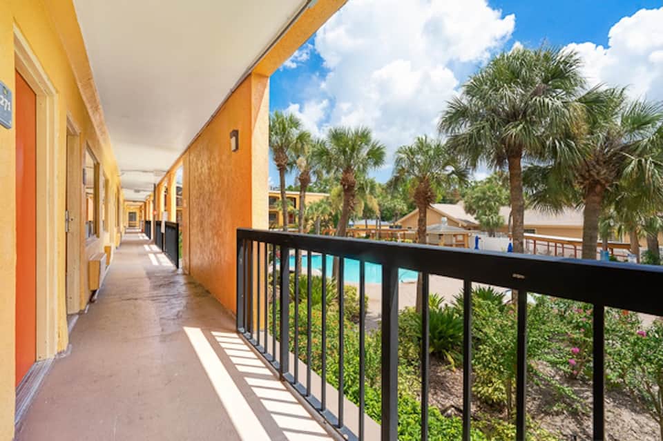 Covered outdoor hallway with orange doors, black railing, and palm trees visible beyond