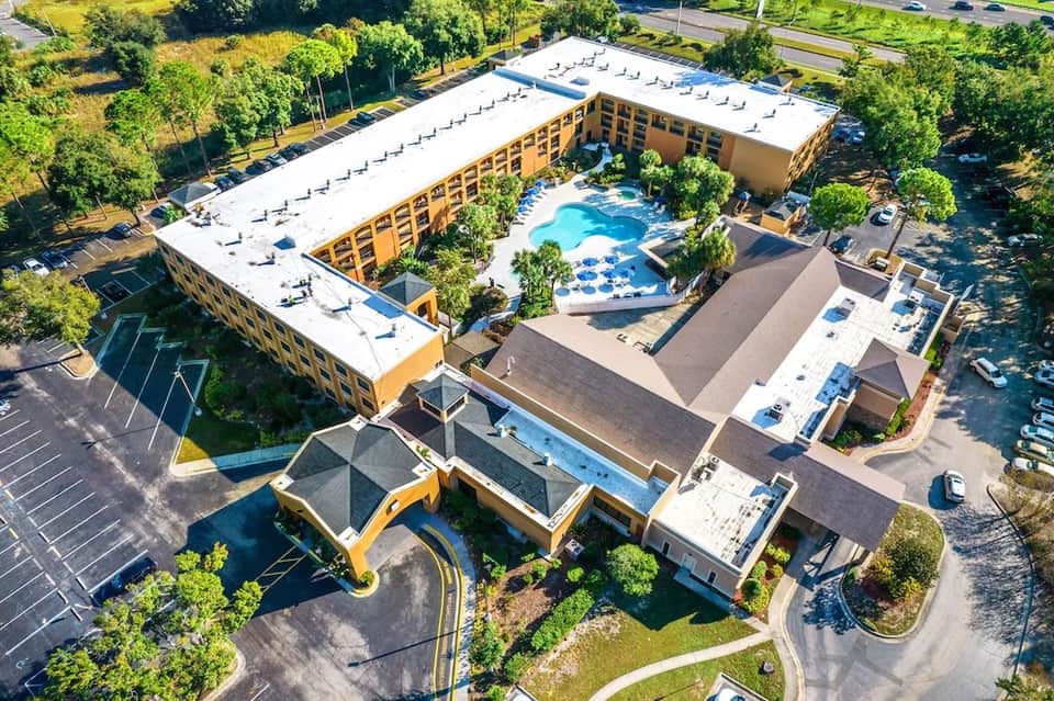 Aerial view of large resort complex with yellow buildings, blue pool area, rooftops, and surrounding landscaping