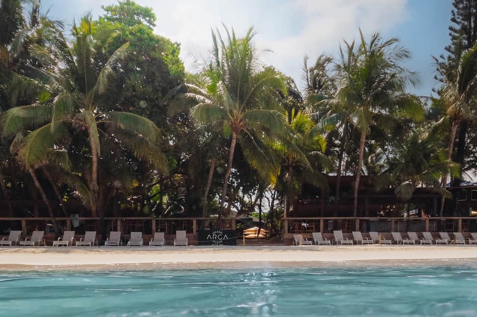 Beachfront resort with palm trees, lounge chairs on sand, and turquoise water