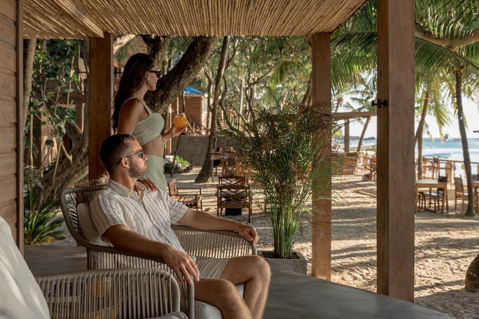Couple relaxing on wooden lounge chairs under pergola with ocean view
