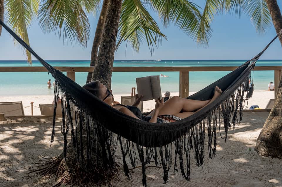 Man relaxing in black hammock between palm trees overlooking tropical beach