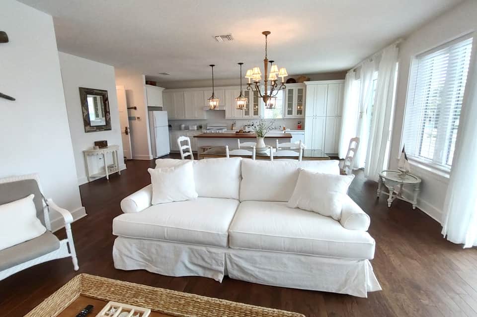 Open-concept condo living room with white sofa, kitchen, and large windows