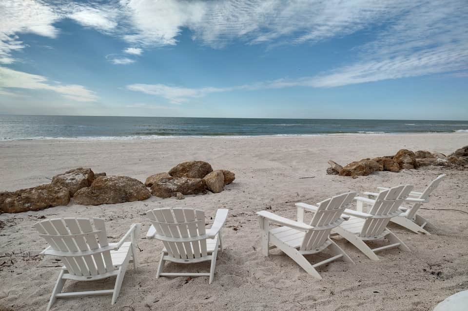 Beach lounge with white Adirondack chairs, ocean view, sandy beach and rock formations