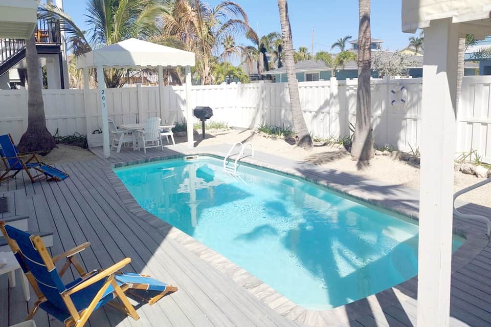 Beach cottage private pool with wooden deck, palm trees, white fence, and lounge chairs