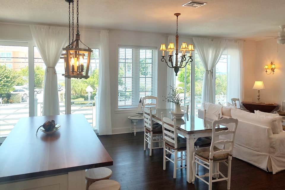Elegant interior living space with chandeliers, white furniture, dark flooring, and large windows