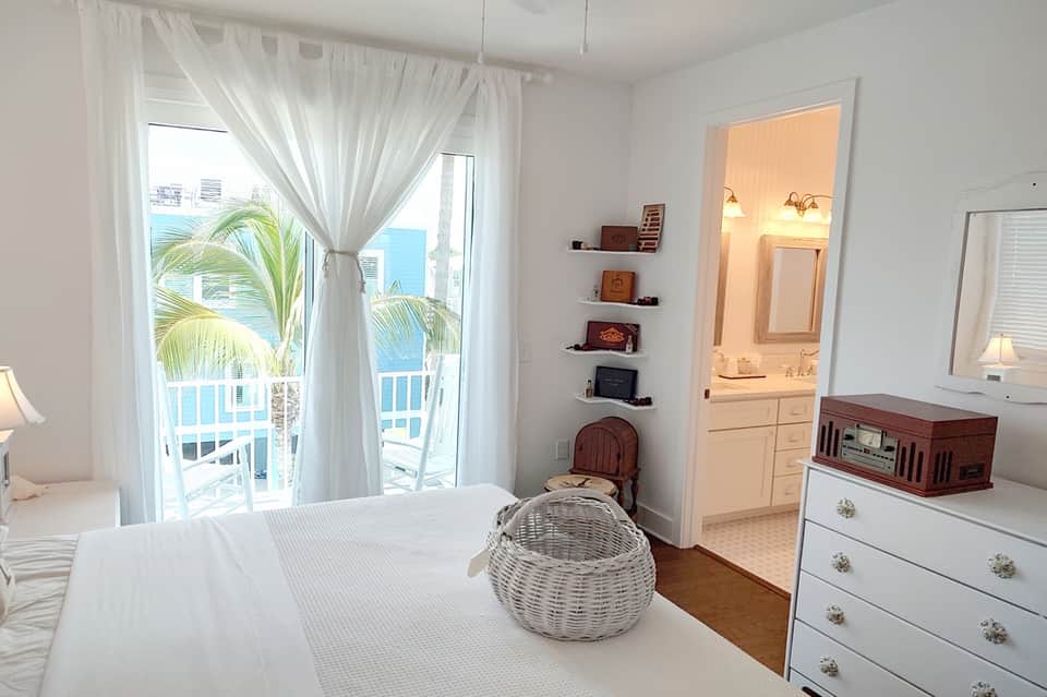 Beachfront bedroom with ocean view, white bed, palm tree views from balcony, and en-suite bathroom