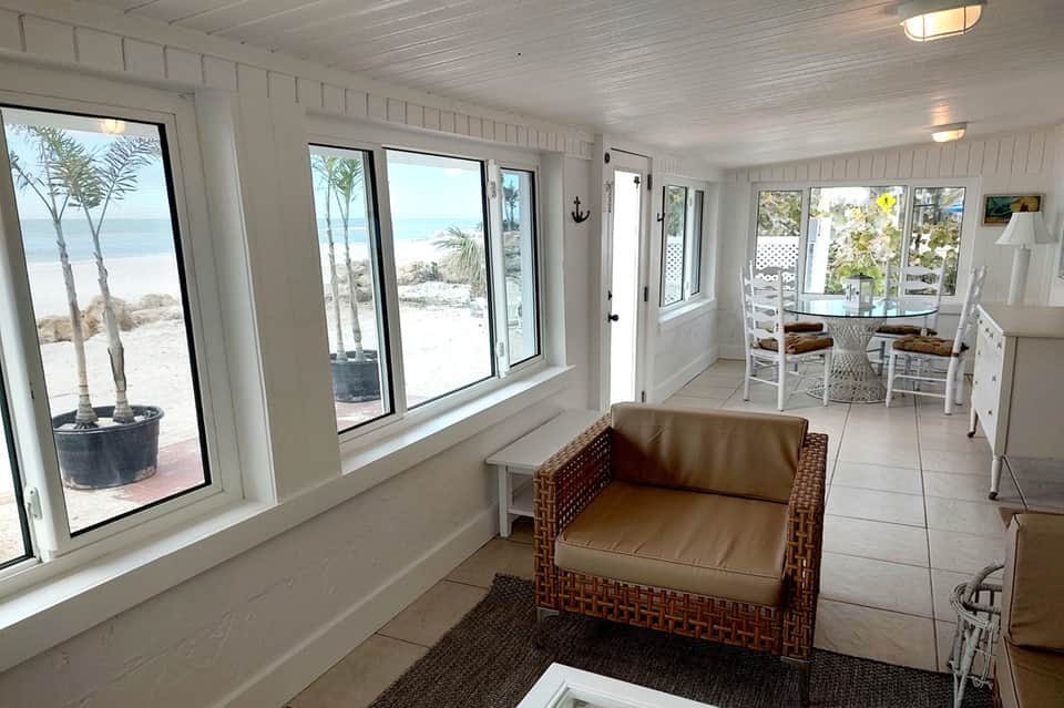 Sunlit beach lounge with wicker seating, ocean view through windows, and casual coastal decor